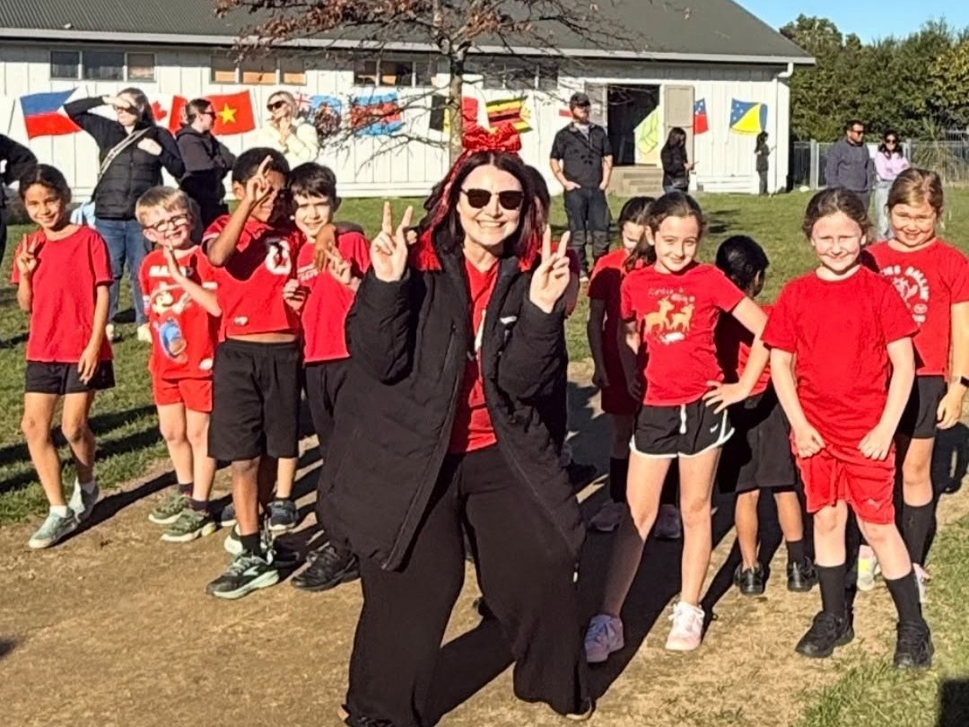 A smiling St Patrick's kaiako and students in red team tops lining up for the school cross country