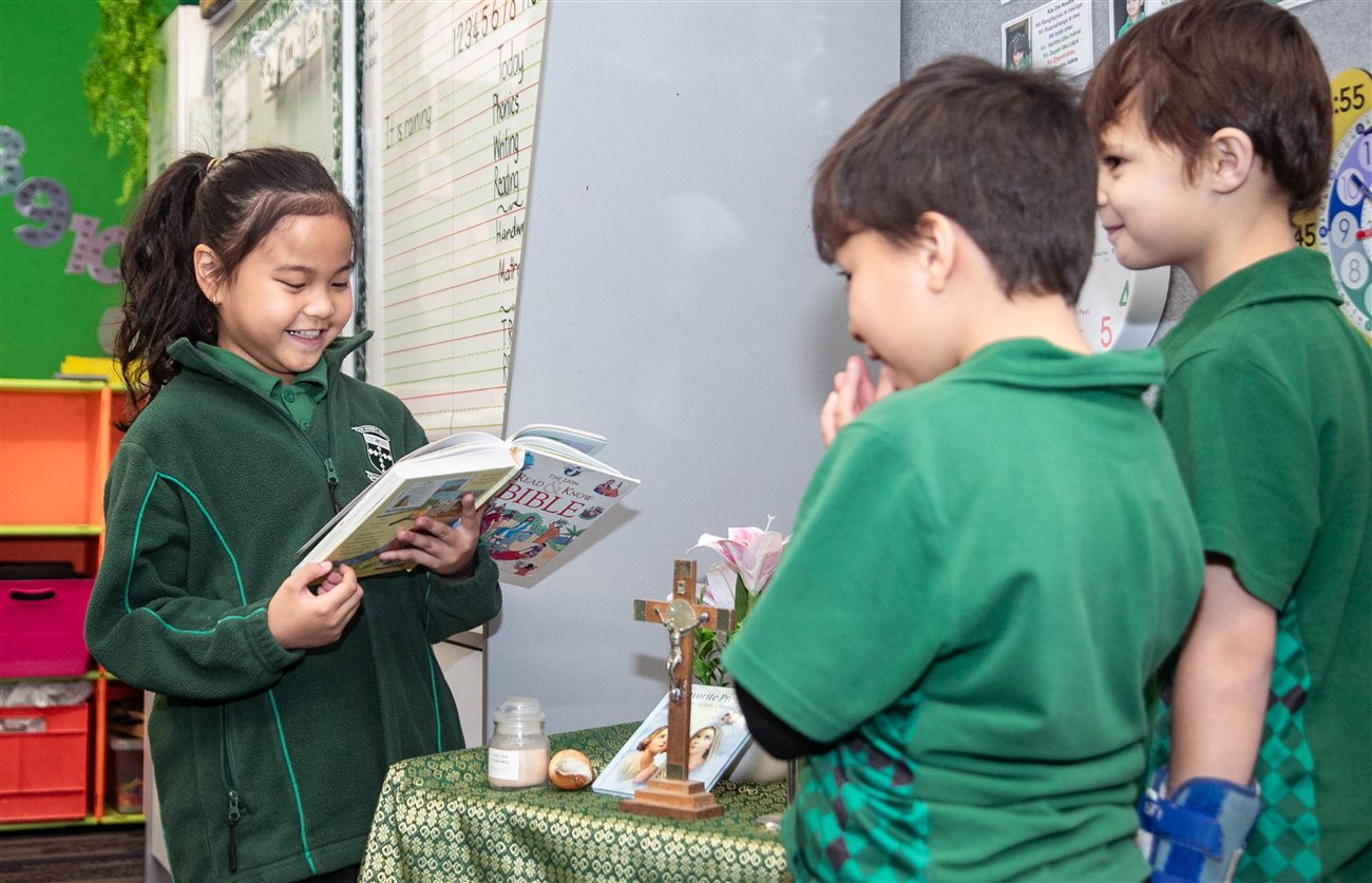 A St Patrick's student reading a Bible beside a small prayer table with a wooden cross and candle, while classmates look on