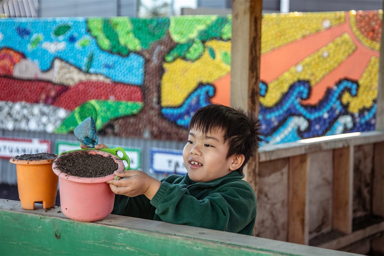 A young St Patrick's student examining potting soil while planting, part of a garden mural backdrop