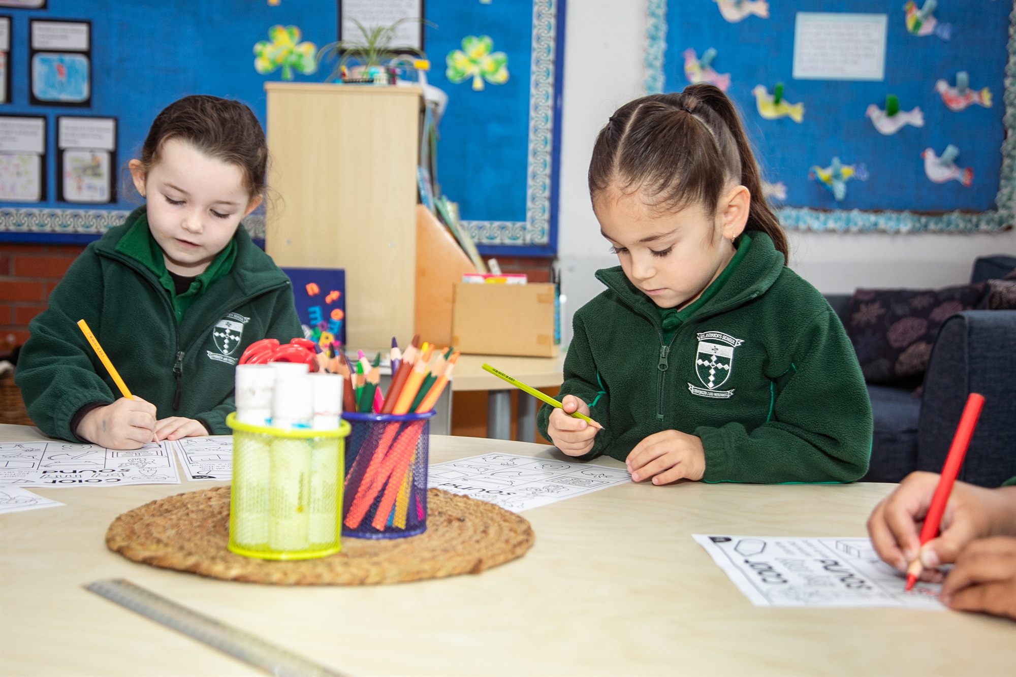 Two young St Patrick's students writing and drawing at a classroom table