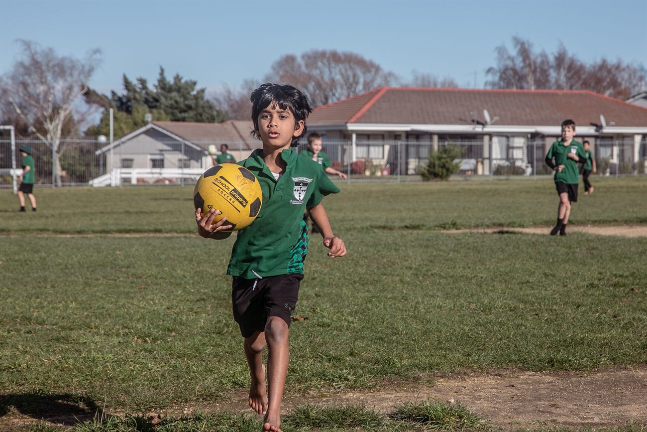 A St Patrick's student running across the school field holding a ball