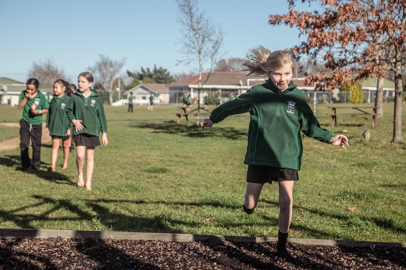 A St Patrick's student kicking a ball across the school field while friends walk behind her
