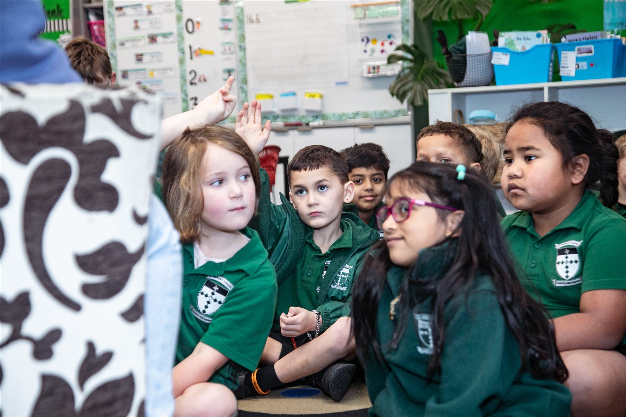 A diverse group of St Patrick's students sitting together on the classroom floor, hands raised