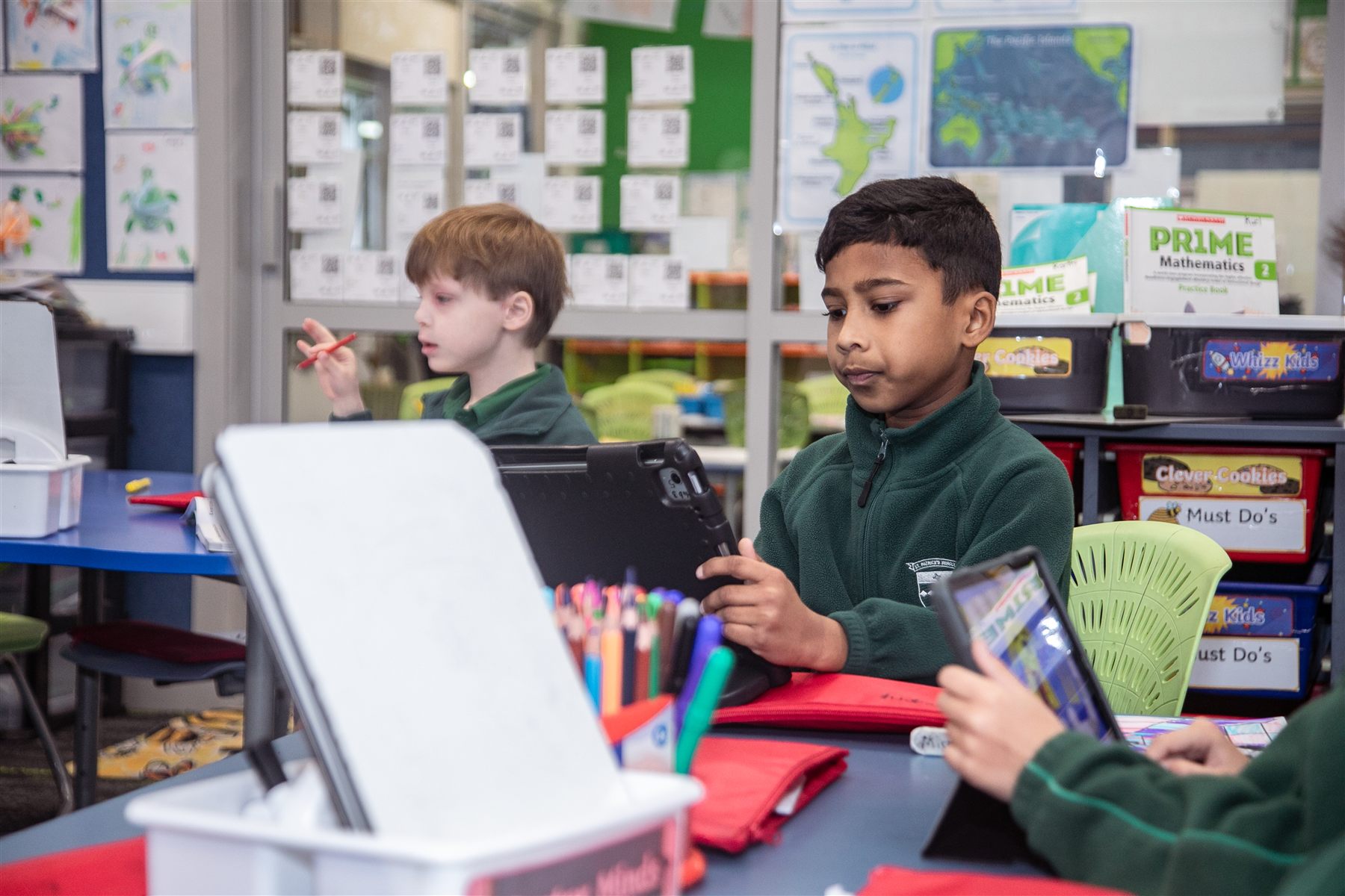 A St Patrick's student smiling as he holds up a tablet at his classroom desk