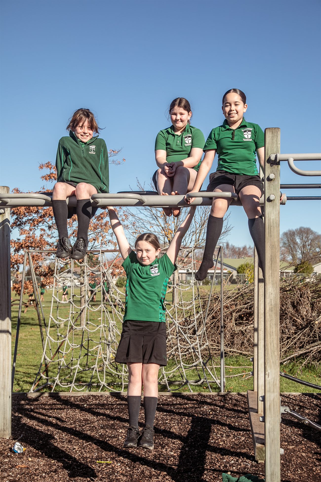 Four St Patrick's girls smiling on the playground climbing frame on a sunny day