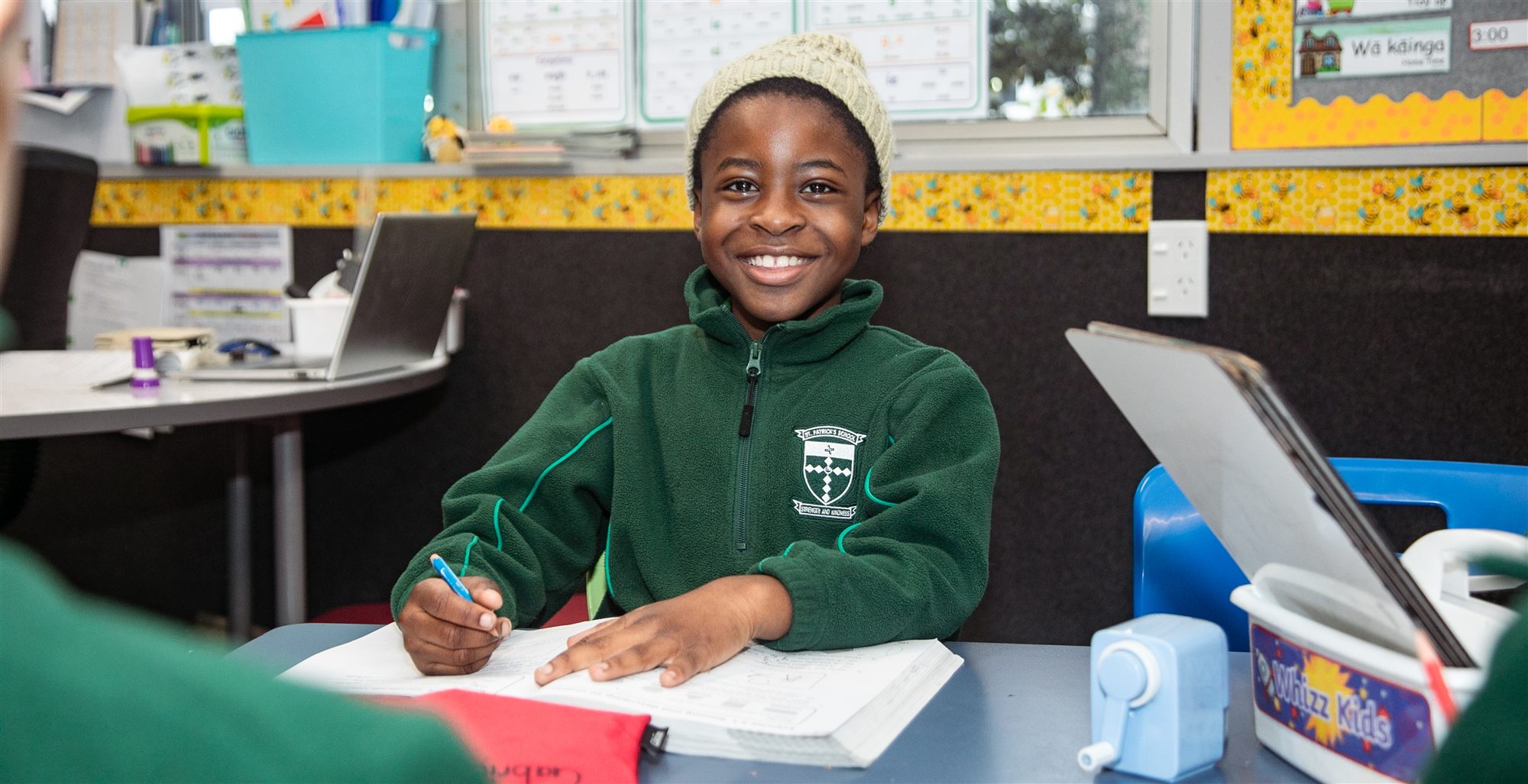 A smiling St Patrick's student writing at his classroom desk