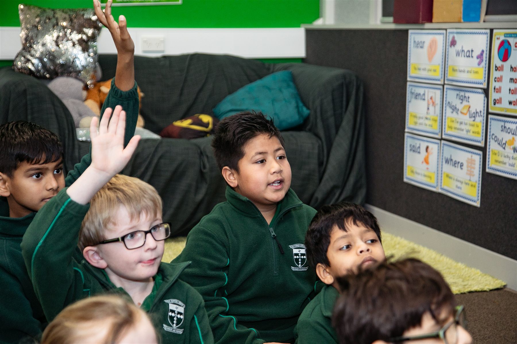 A group of St Patrick's students on the classroom floor, hands raised to answer a question