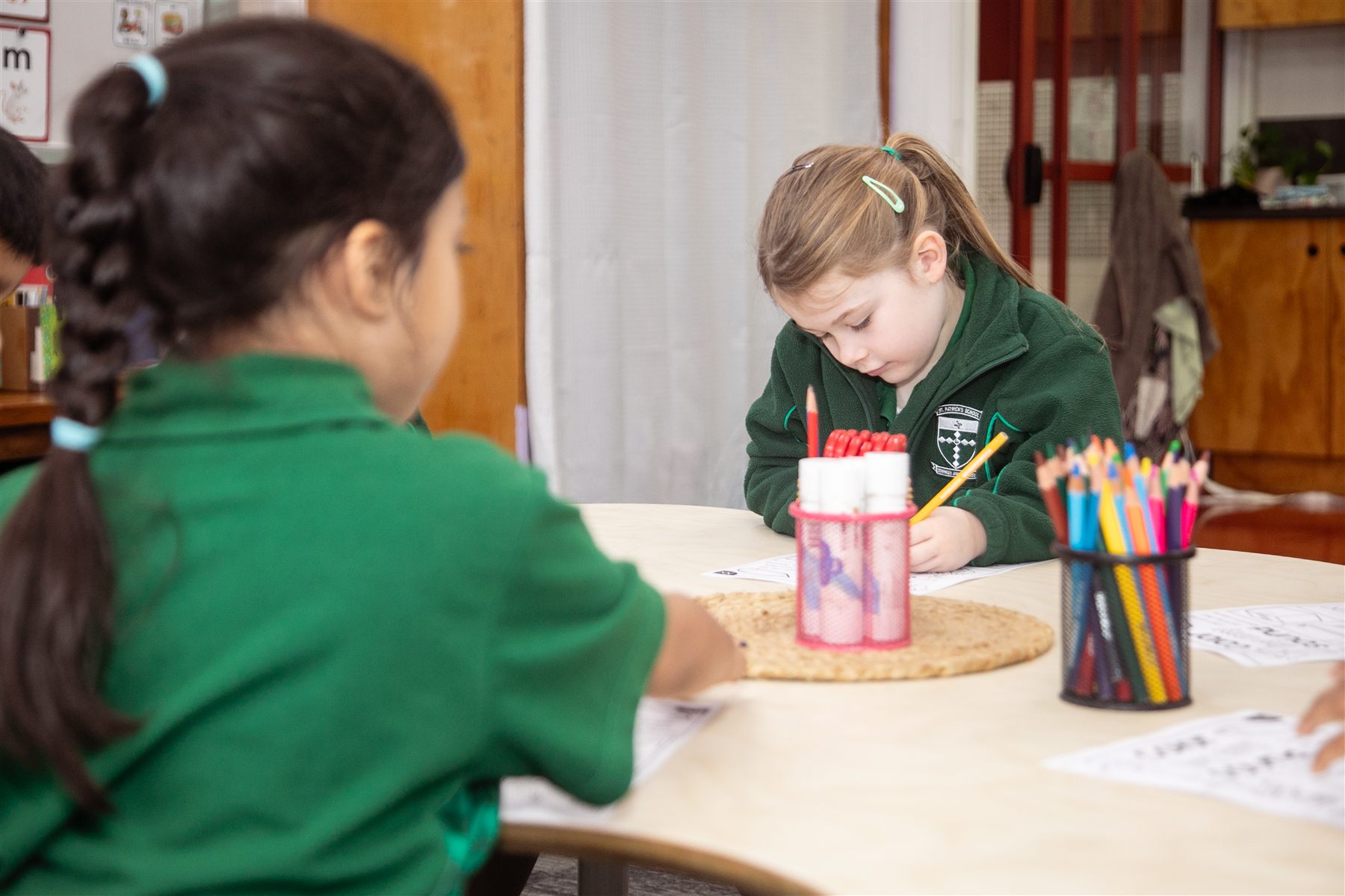 A St Patrick's student concentrating as she draws at a classroom table, with coloured pencils beside her