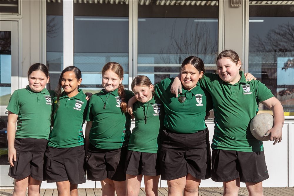 Six girls in school uniform standing arm in arm, laughing together