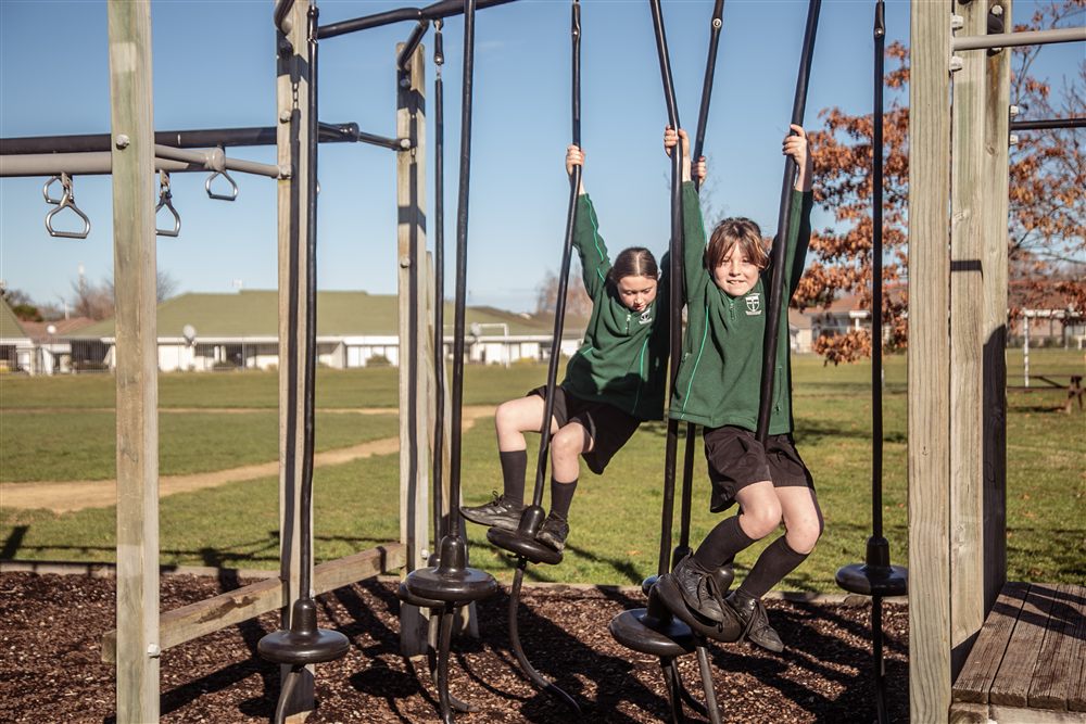 Two girls hanging from the wooden climbing frame on the school playground